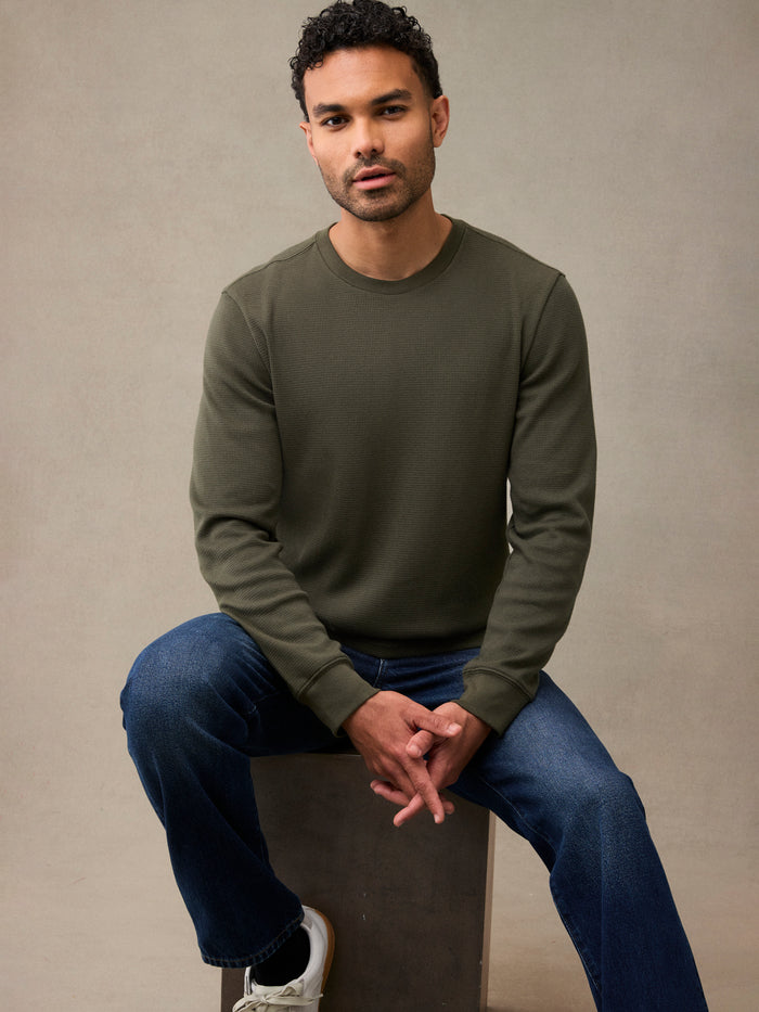 A man wearing an army green waffle flannel and blue jeans, sitting. A better thermal for a great price.