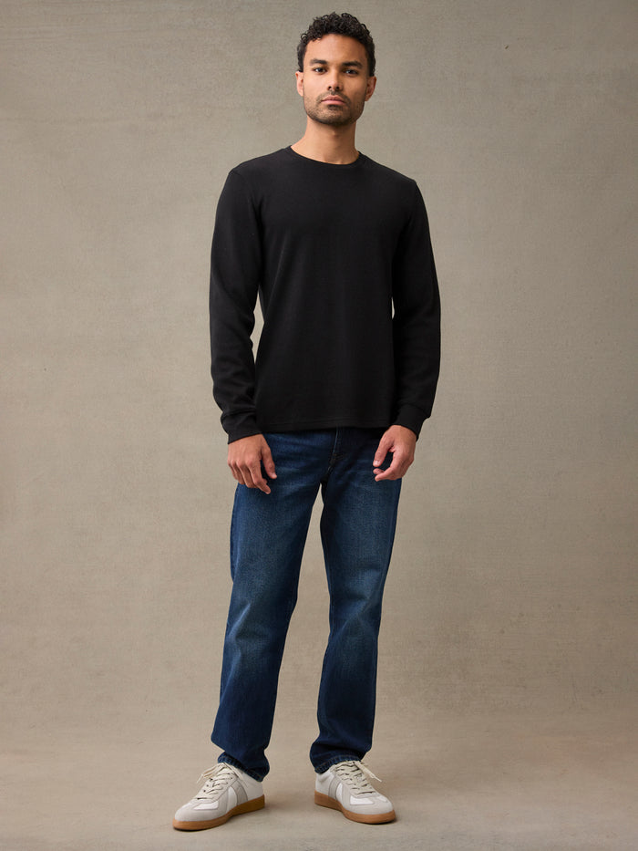 A man wearing a black long-sleeve flannel shirt, dark blue jeans, and white sneakers. 280 GSM waffle knit traps warmth without overheating