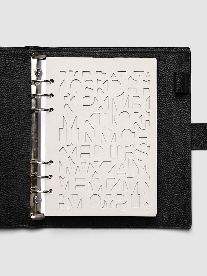 The A5 6-Ring Punch Diecut Pocket Folder empty at the front of a black leather ring bound planner, the cut letters showing the blank page beneath