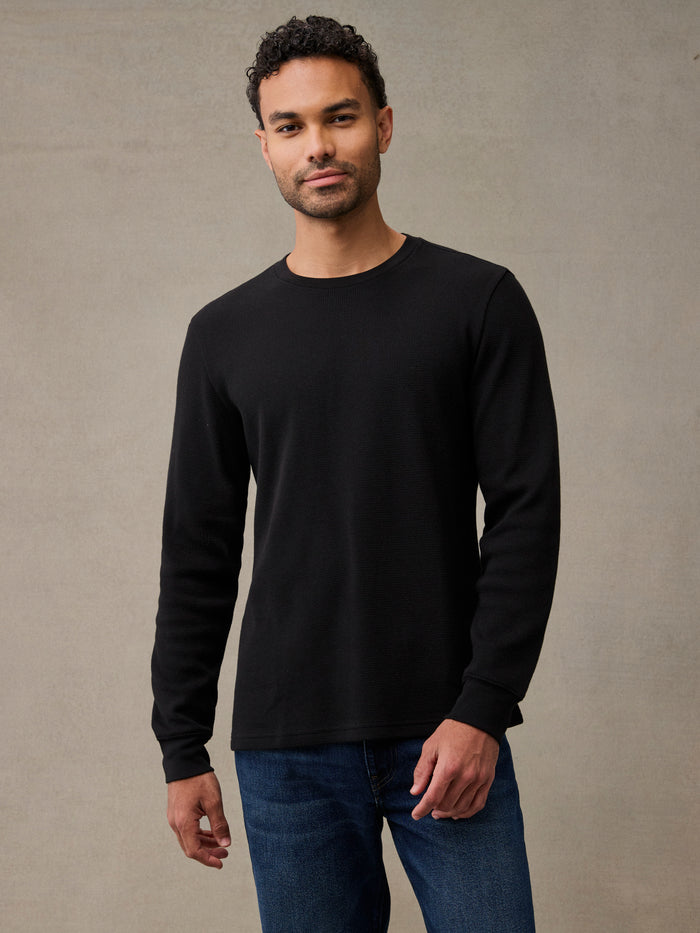 A man wearing a black long-sleeve flannel shirt and blue jeans. The thermal that keeps up with the whole weekend.