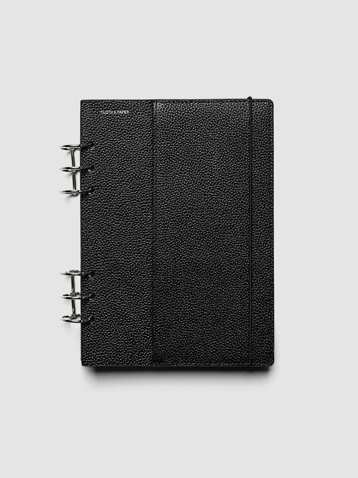 The A5 6-Ring Punch Genuine Leather Planner Cover Set closed on a ring bound planner, showing the silver rings, the silver foiled logo, and the bungee cord holding the stack shut