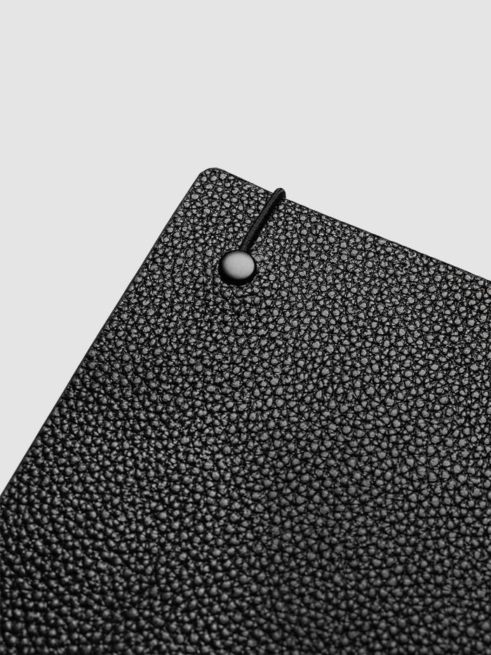 Close-up of the top corner of the A5 6-Ring Punch Genuine Leather Planner Cover Set, showing the bungee cord anchored to the black leather with a silver metal stud