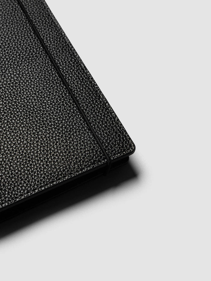 Close-up of the corner of the A5 6-Ring Punch Genuine Leather Planner Cover Set with the bungee cord running along the edge of the pebbled black leather
