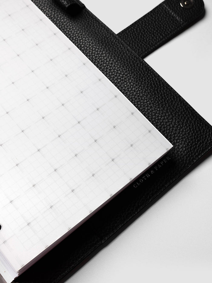 Grid Top Tab Dividers | Ultra-Thin, A5 6-Ring Punch, angled close-up of the outer edge of a divider resting on black pebbled leather, with the Cloth & Paper mark printed along the edge
