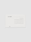 Pocket Calendar | October 2026, a small off white card printed in soft gray with the month name at the left, a full grid of dates under single letter weekday headers, and the year set at the lower left