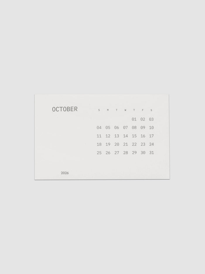 Pocket Calendar | October 2026, a small off white card printed in soft gray with the month name at the left, a full grid of dates under single letter weekday headers, and the year set at the lower left