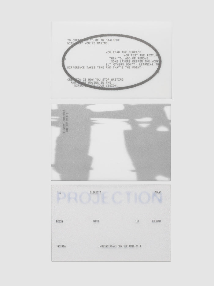 Projection Journaling Card Set, three cards stacked in a column on a light gray background, one white with gray type inside a wide gray oval, one covered edge to edge in a blurred gray and white image, one pale gray with soft blue lettering behind scattered black type