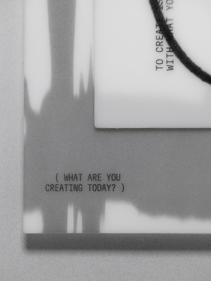 A close-up of a journaling card set with black printed text reading '( WHAT ARE YOU CREATING TODAY? )' and a black cord wrapped around the corner, shown against a gray background.
