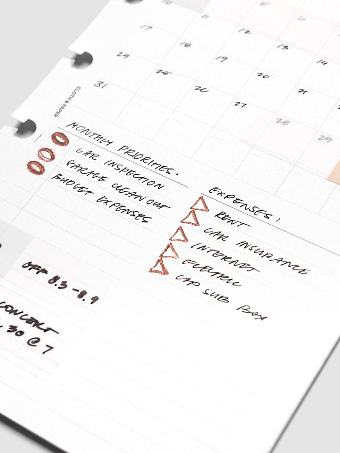 Stamp Sticks | Set of 2 in use on a white monthly planner page, rust colored oval and triangle impressions stamped beside handwritten priority and expense lists in black ink