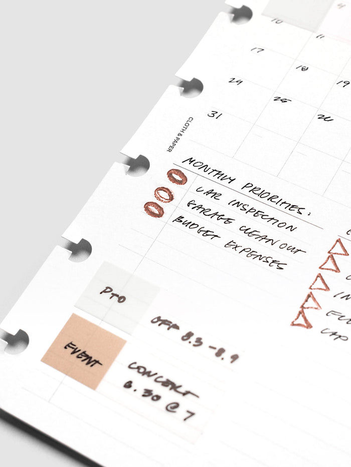 Stamp Sticks | Set of 2 in use, a discbound white monthly page shot at a low angle with rust colored oval and triangle impressions marking handwritten entries beside a tan event tab