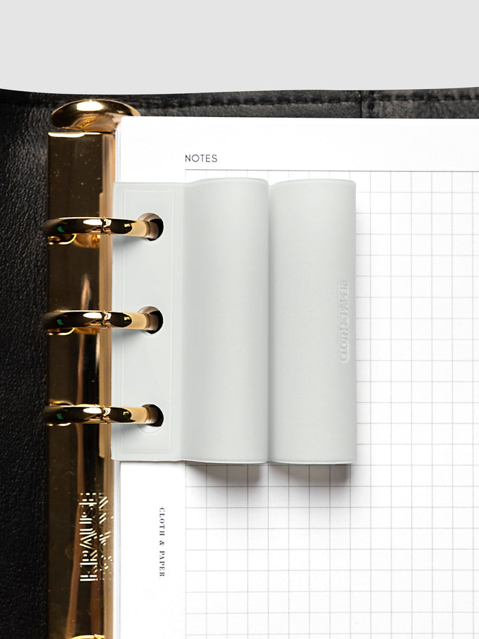System Punch Pen Holder | Aspen, ring punch, pale gray holder threaded onto gold rings in a black leather binder over a white grid notes page
